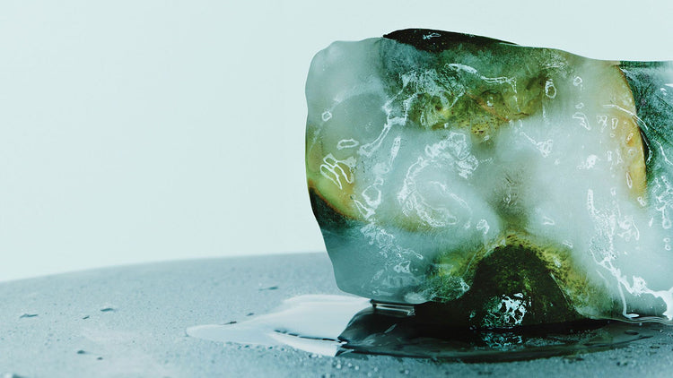 Photo of the inside of an avocado cut into half frozen in ice melting on table surface