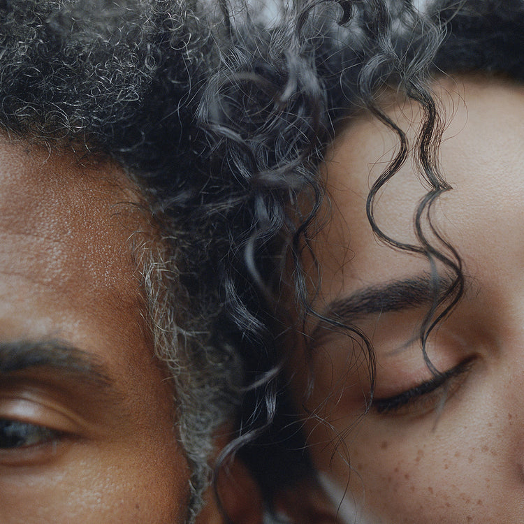Photo of a man and women with dark curly afro hair leaning their heads against each other
